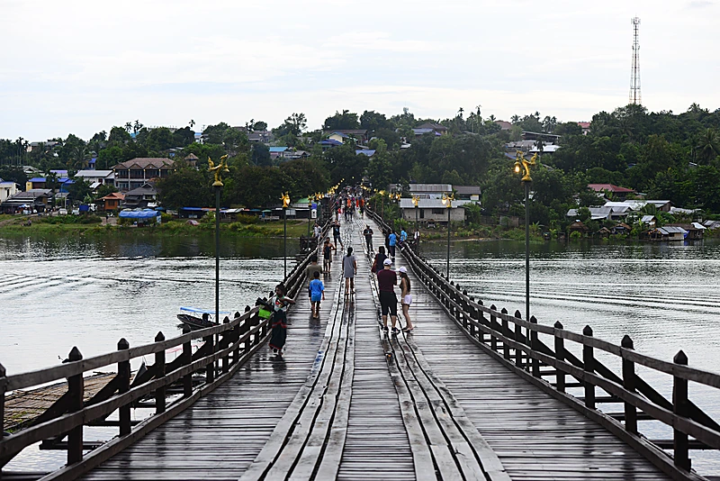 ผู้คนเดินข้ามสะพานมอญ สะพานไม้ที่ยาวที่สุดในไทย ยามเช้า